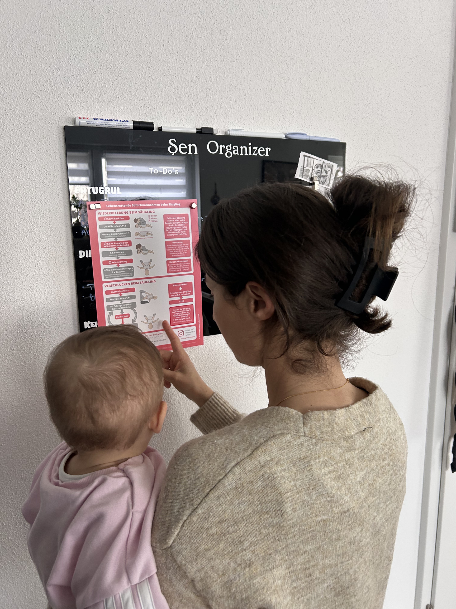 Mutter mit Kind in der Küche neben aufgehängtem Notfallplan